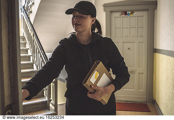 Confident delivery woman with package standing at doorstep
