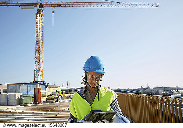 Confident female architect in reflective clothing using digital tablet at construction site against clear sky