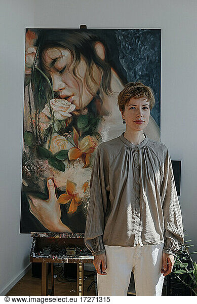 Confident female artist standing against painting in art studio