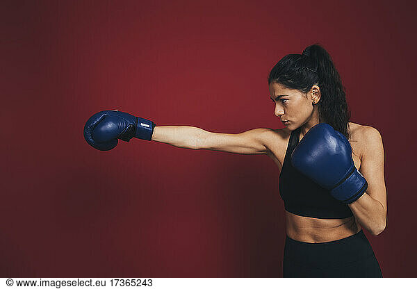 Confident female athlete practicing punches in front of maroon wall