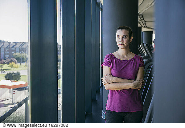 Confident female athlete with arms crossed standing by window in gym