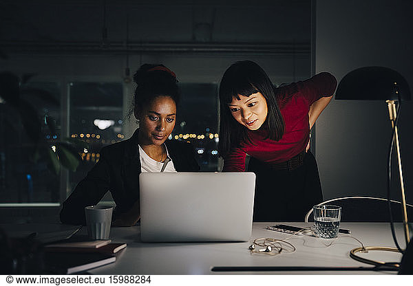 Confident female business colleagues discussing over laptop while working late at creative office