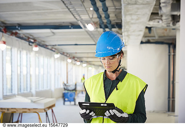 Confident female engineer in reflective clothing using digital tablet at construction site