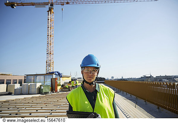 Confident female engineer in reflective clothing with digital tablet at construction site against clear sky