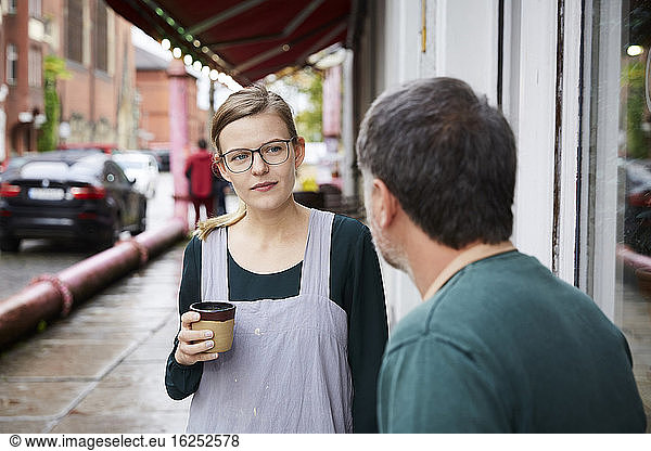 Confident female having coffee with male coworker outside art studio