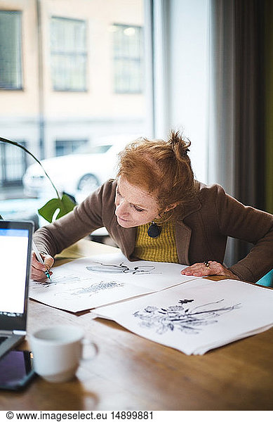Confident female illustrator drawing on paper at table in office