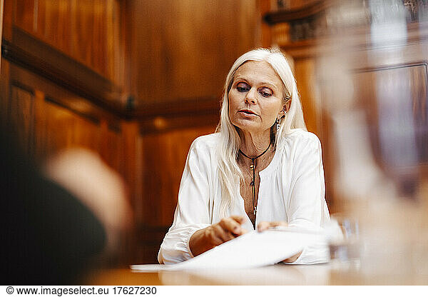 Confident female lawyer sitting with contract document in board room