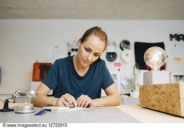 Confident female technician working at workbench while sitting in creative office