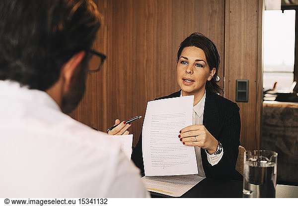 Confident lawyer discussing over document with male client at law office