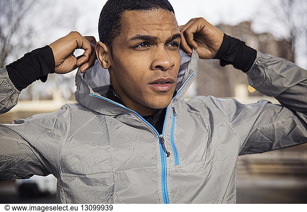Confident male athlete wearing hooded jacket outdoors