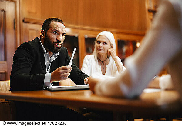 Confident male financial advisor discussing over contract document with female colleagues in board room