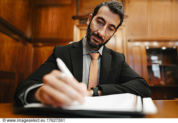 Confident male financial advisor signing contract document in board room during meeting