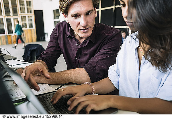 Confident male IT professional discussing with female hacker using laptop at desk in creative office