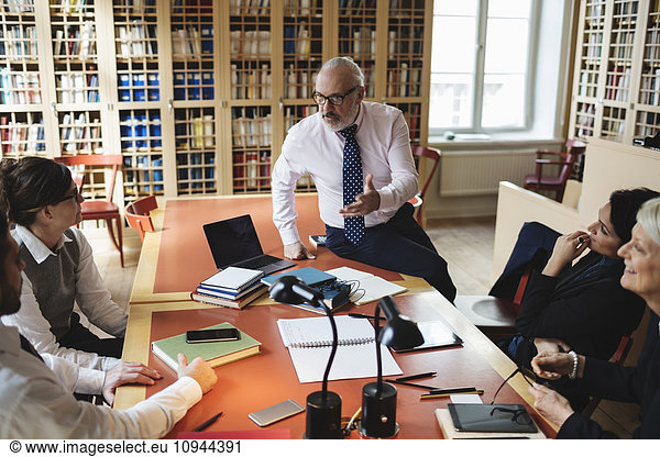 Confident male professional discussing with coworkers sitting at table in law library