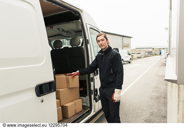Confident manual worker standing by stack of boxes in delivery van