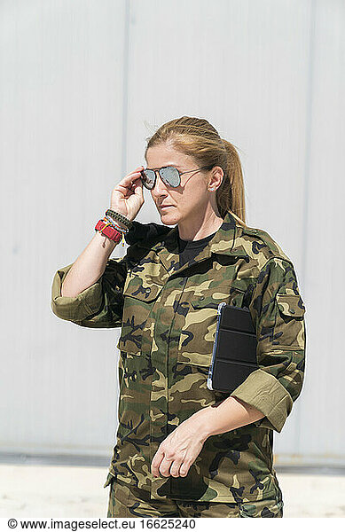 Confident mature blond female army soldier wearing sunglasses at military base on sunny day