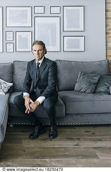 Confident mature businessman wearing suit sitting on sofa at home