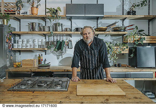 Confident mature chef staring while standing by kitchen counter in kitchen