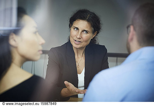 Confident mature female financial advisor discussing with businessman and businesswoman during meeting at office