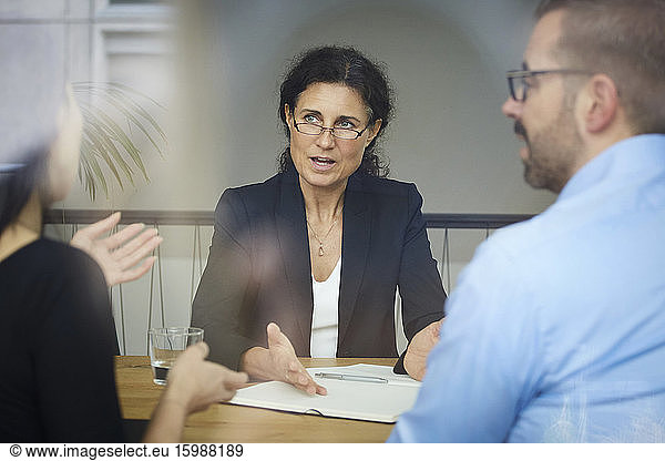Confident mature female lawyer discussing with businessman and businesswoman during meeting at office