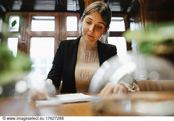 Confident mature female lawyer signing contract document in board room