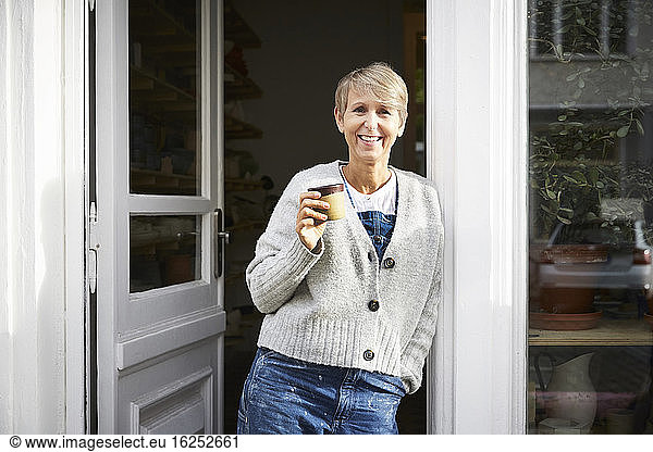 Confident mature woman having coffee at entrance of art studio