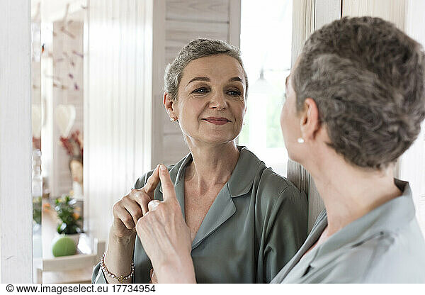 Confident mature woman looking in mirror at home