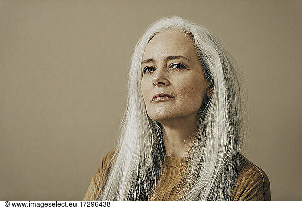 Confident mature woman with white hair against beige background