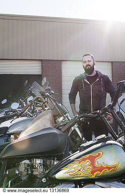 Confident mechanic standing by motorcycles outside shop