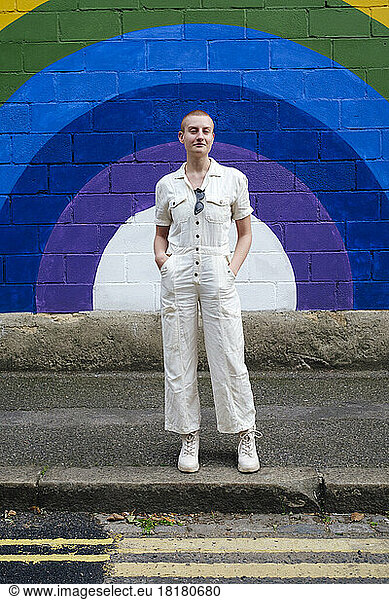 Confident non binary person standing on footpath in front of wall