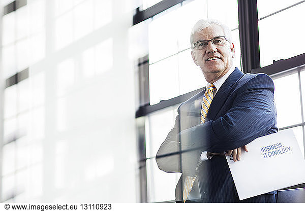 Confident senior man standing with document in office