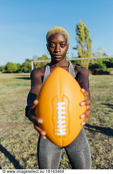 Confident sports player holding American football in field