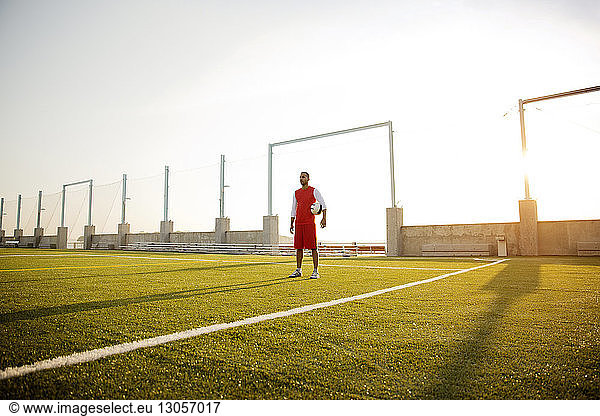 Confident sportsman standing on soccer field during sunny day