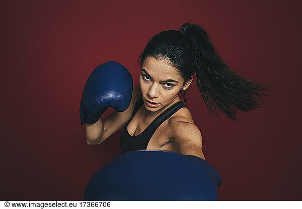 Confident sportswoman boxing against maroon background