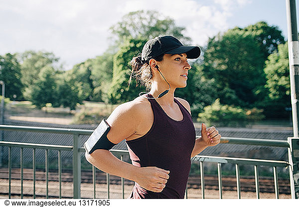 Confident sportswoman listening music while jogging on bridge in city