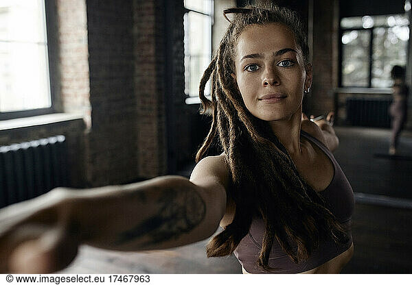 Confident sportswoman with locs hairstyle exercising Warrior Pose in yoga studio