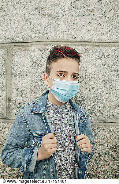 Confident teen boy wearing mask red highlights hair and denim by wall