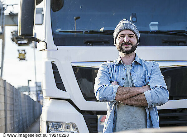 Confident truck driver with arms crossed standing in front of truck