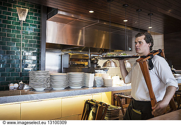 Confident waiter holding dish while walking in commercial kitchen