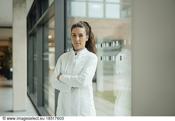 Confident woman in lab coat standing with crossed arms near window