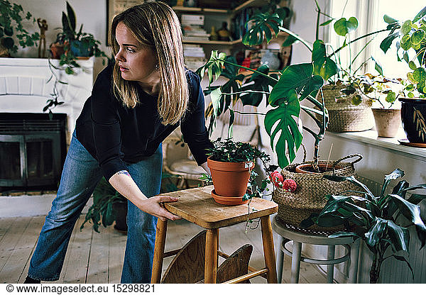 Confident woman positioning stool and potted plant in room at home