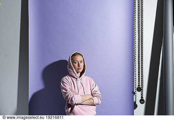 Confident woman with arms crossed wearing hooded shirt against purple background