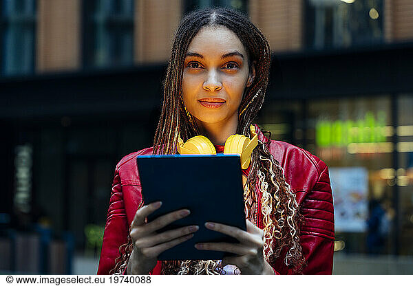 Confident woman with braided hair holding tablet PC