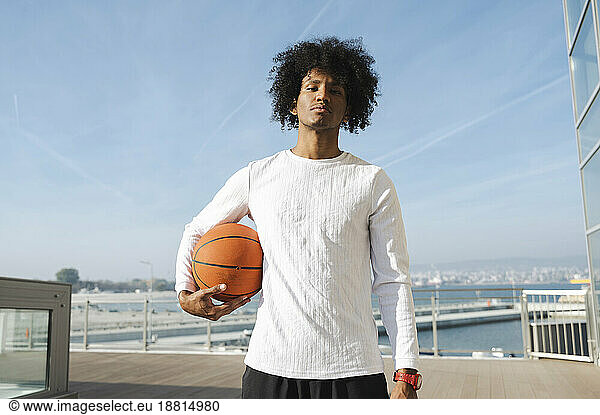 Confident young athlete holding basketball at sunny day