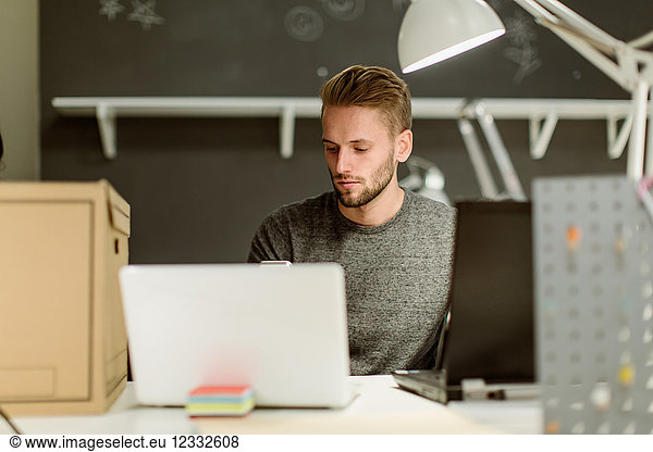 Confident young businessman using laptop while sitting at desk in creative office