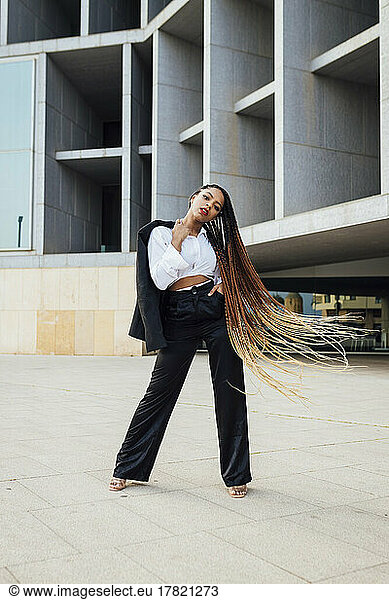 Confident young businesswoman with long braided brown hair standing in front of office building