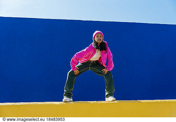 Confident young dancer wearing pink jacket dancing on wall