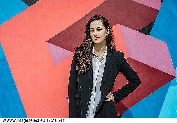 Confident young female manager standing near graffiti wall
