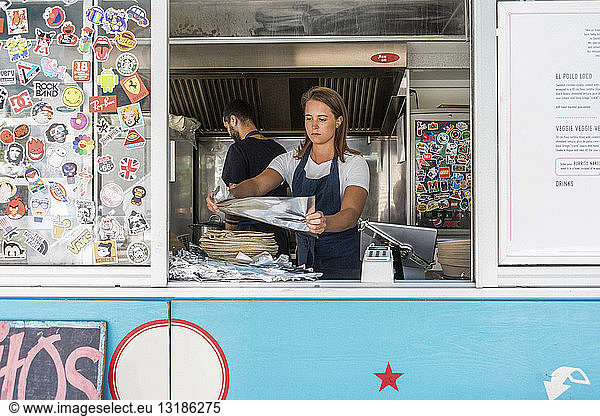 Confident young female owner holding foil against colleague working in food truck