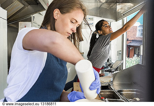 Confident young female owner preparing food while colleague working in food truck